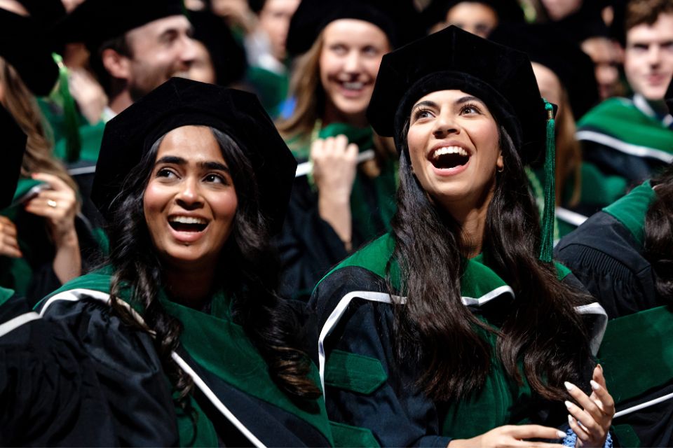 Two medical school graduate in caps and gowns smile at the crowd during the precommencement ceremony.