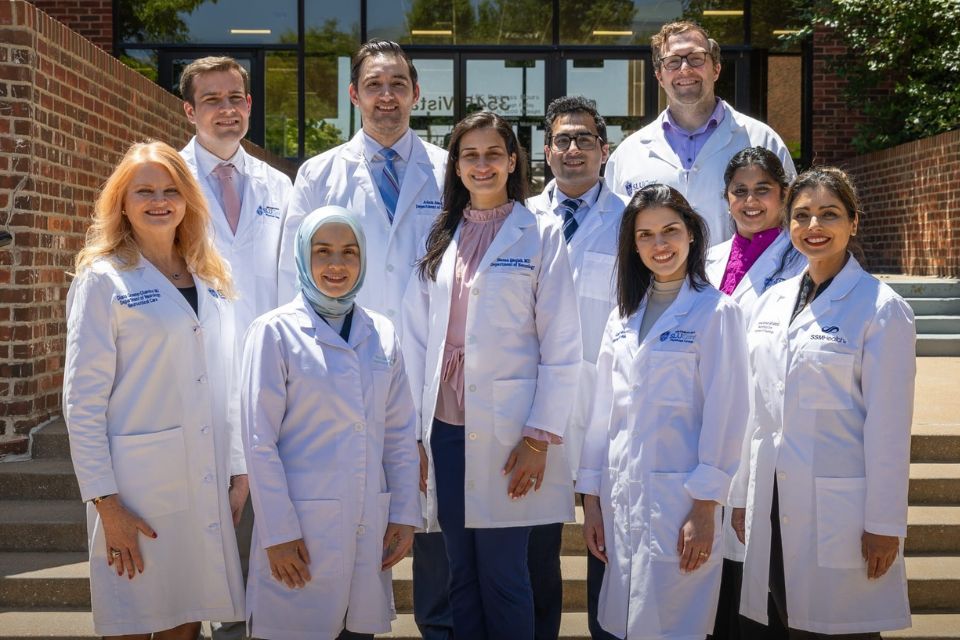 2026 Graduates A group photo of 2026 neurology graduates in white coats standing outside a brick building entrance