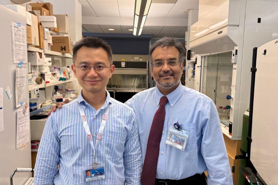 Two smiling doctors stand shoulder to shoulder inside a laboratory.