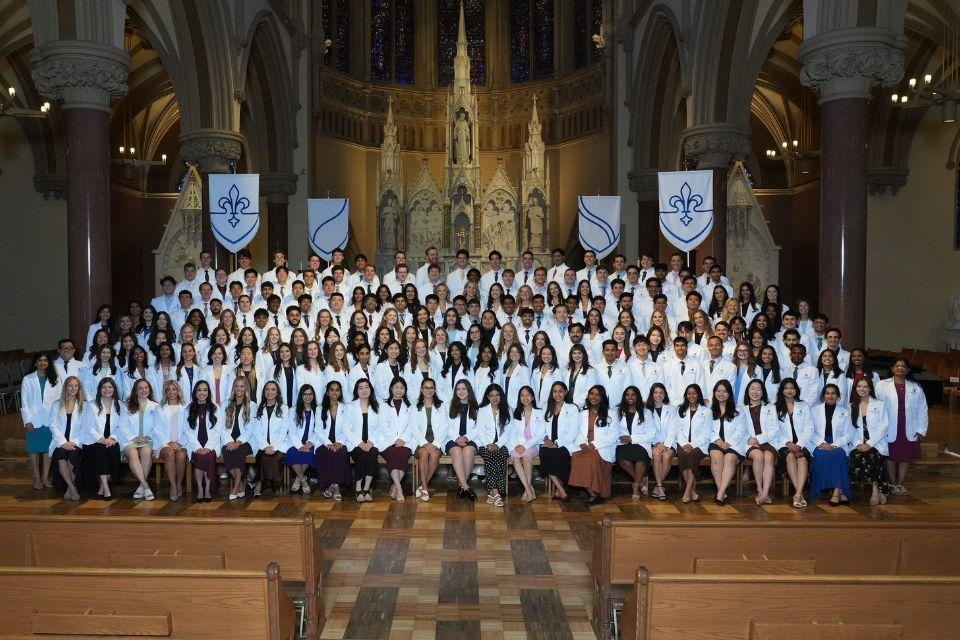 SLU SOM's incoming medical students pose together in white coats at the altar inside a historic Catholic church.