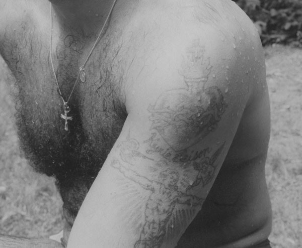 A detail of a black-and-white photo of Adrian Kellard showing tatoos on his upper left arm.