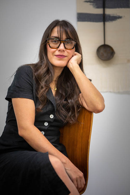 Artist Jenelle Esparza sits in front of one of her tapestry artworks