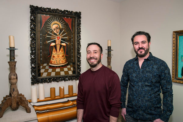 Artists Vicente Telles and Brandon Maldonado stand in front of a painting of Our Lady of Sorrows in a MOCRA side chapel gallery