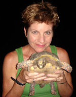 Dancer Jude Woodcock smiles as she holds a turtle in front of her.
