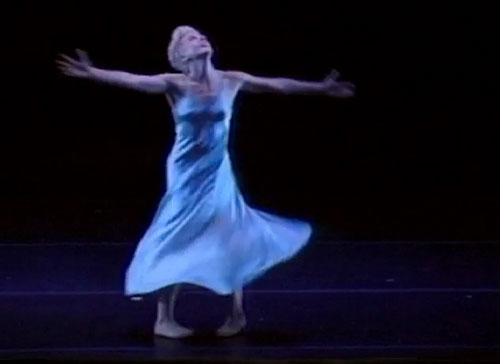 Dancer Jude Woodcock pictured in a moment from the dance Moonblind. Her arms outstretched, she looks up, her white dress twisting and billowing around her.
