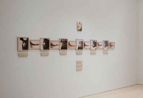 An artwork by Maria Magdalena Campos-Pons titled, Umbilical Cord. Twelve photos in a horizontal row alternate pictures of women's abdomens with a white cross over their belly buttons, with an outstretched hand holding a string connected to the cross.