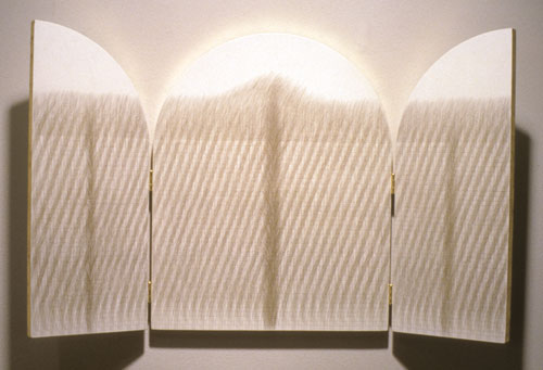 An artwork by Susan Schwalb titled Sacred Land IV. Two panels unfold on hinges from a central, tablet-shaped panel. The three panels are painted white and covered with a dense network of fine lines hand-drawn in silverpoint and gold.