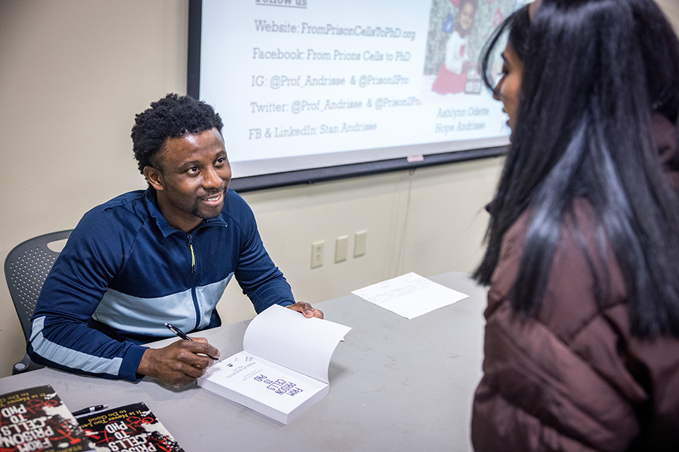 A photo of Dr. Stanley Andrisse signing a copy of his book. He speaks to a woman with long, black hair.