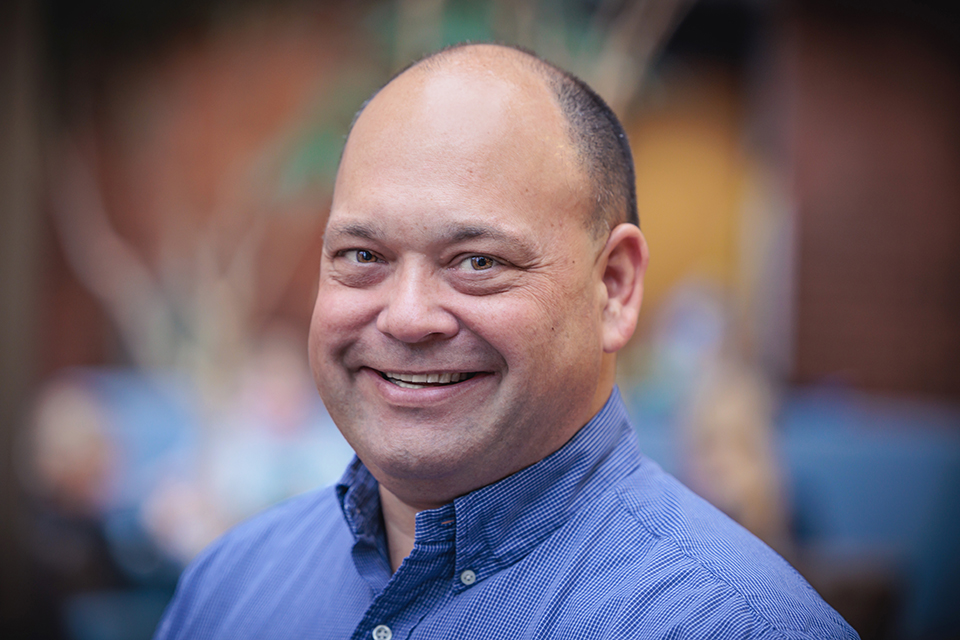 Chris Hemmer smiles at the camera. He wears a ligh-blue shirt.