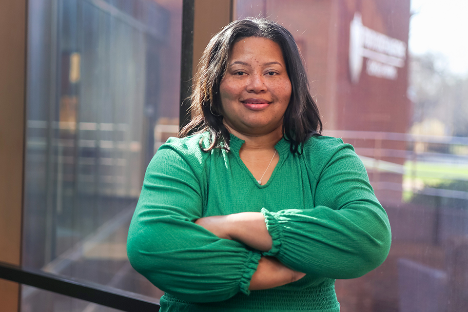 Devita Stallings is photographed indoors. She folds her arms across her chest and poses for the camera. She wears a green shirt.