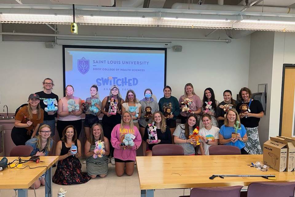 A group of people holding toys pose for a photo inside a classroom.