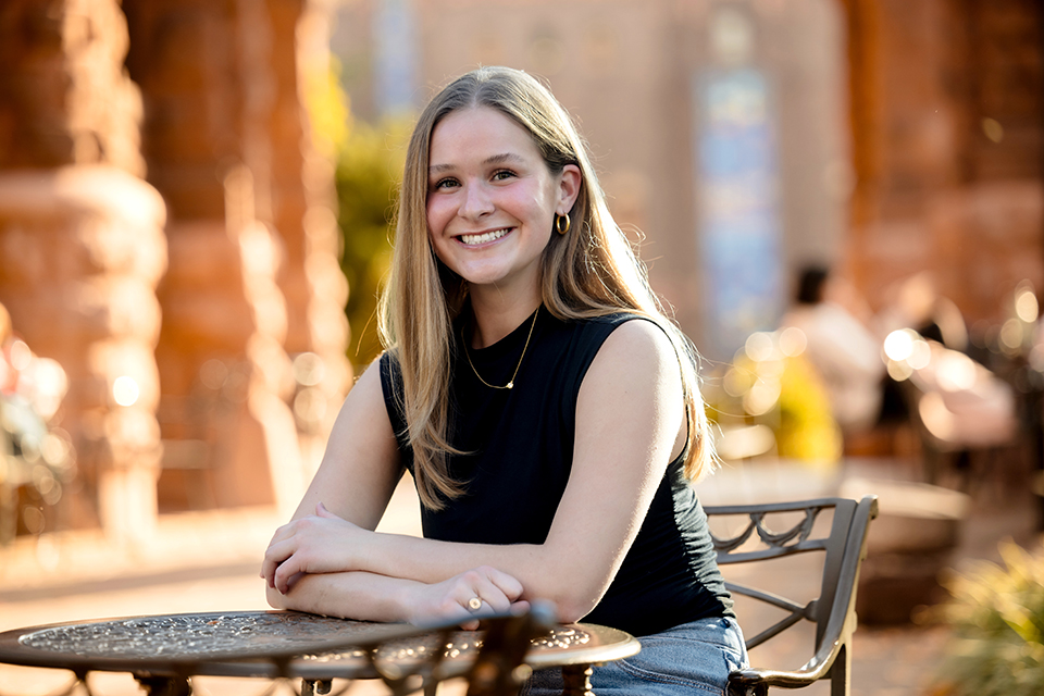 A photo of Lucy Heller sitting at an outdoors table on a fall day.