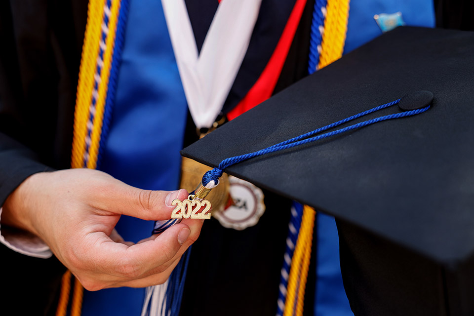Close up of a graduation cap with a charm reading 2022 held in the hand of an unseen student