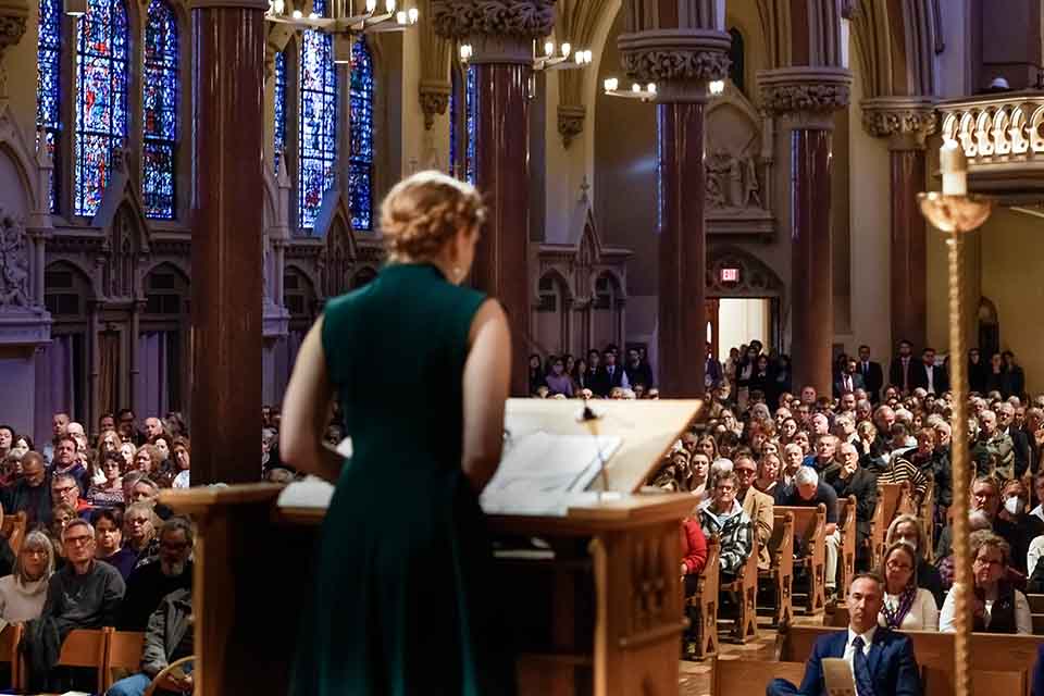 A woman wearing a green dress addresses an audience at St. Francis Xavier College Church.