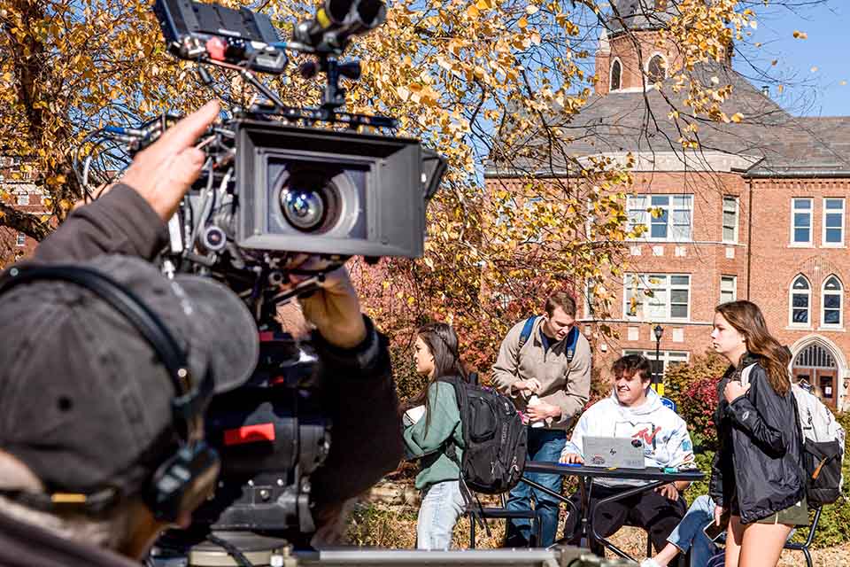 Students pass behind cameras during filming of the commencement scene of “On Fire,” a movie based on alum John O’Leary’s life, on November 10, 2023.