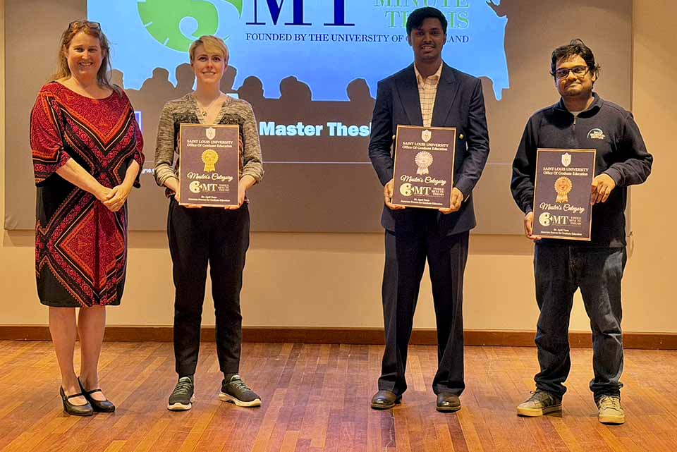 four people stand on a stage. three are holding plaques