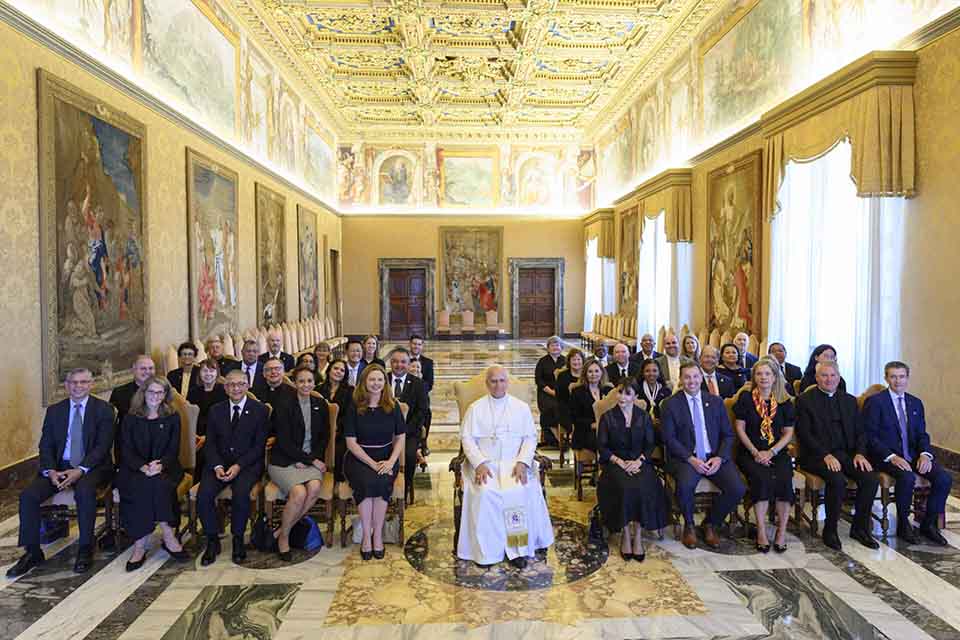 A group of professionally dressed leaders from Jesuit colleges and universities poses for a photo with Pope Leo XIV, wearing a white papal floor-length robe and cap. They are in an ornate room with a decorated ceiling and large paintings at the Apostolic Palace in Rome. A group of professionally dressed leaders from Jesuit colleges and universities poses for a photo with Pope Leo XIV, wearing a white papal floor-length robe and cap. They are in an ornate room with a decorated ceiling and large paintings at the Apostolic Palace in Rome.