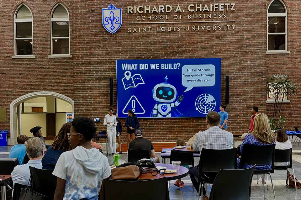 a group of people sitting at tables in front of a large screen