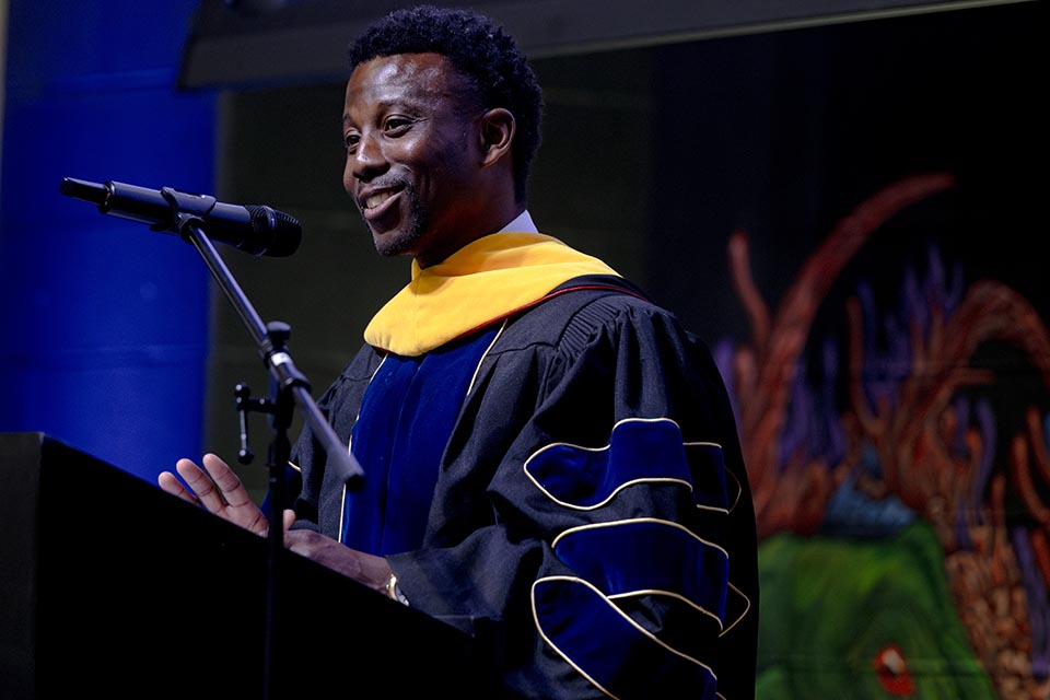 a man in graduation garb speaks to graduates