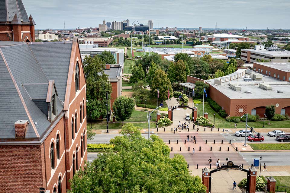 An aerial campus view showing part of the slate roof of DuBourg Hall and pedestrians crossing Grand Boulevard nearby. 