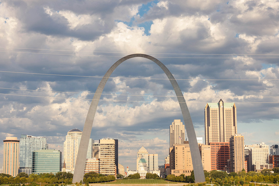 A view of the Gateway Arch and the City of St. Louis skyline with a partially cloudy sky.