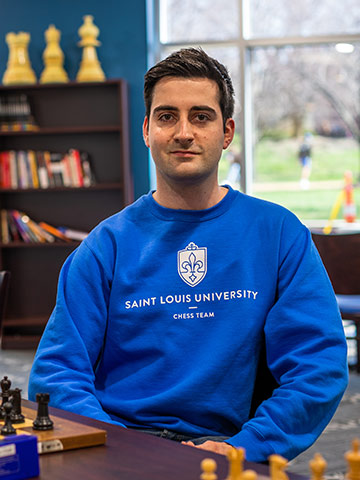 Saint Louis University Chess Team member and Grandmaster Benjamin Bok sitting in front of a chess board wearing a blue SLU sweatshirt. Saint Louis University Chess Team member and Grandmaster Benjamin Bok sitting in front of a chess board wearing a blue SLU sweatshirt.