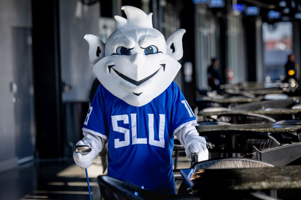 Billiken holds golf clubs