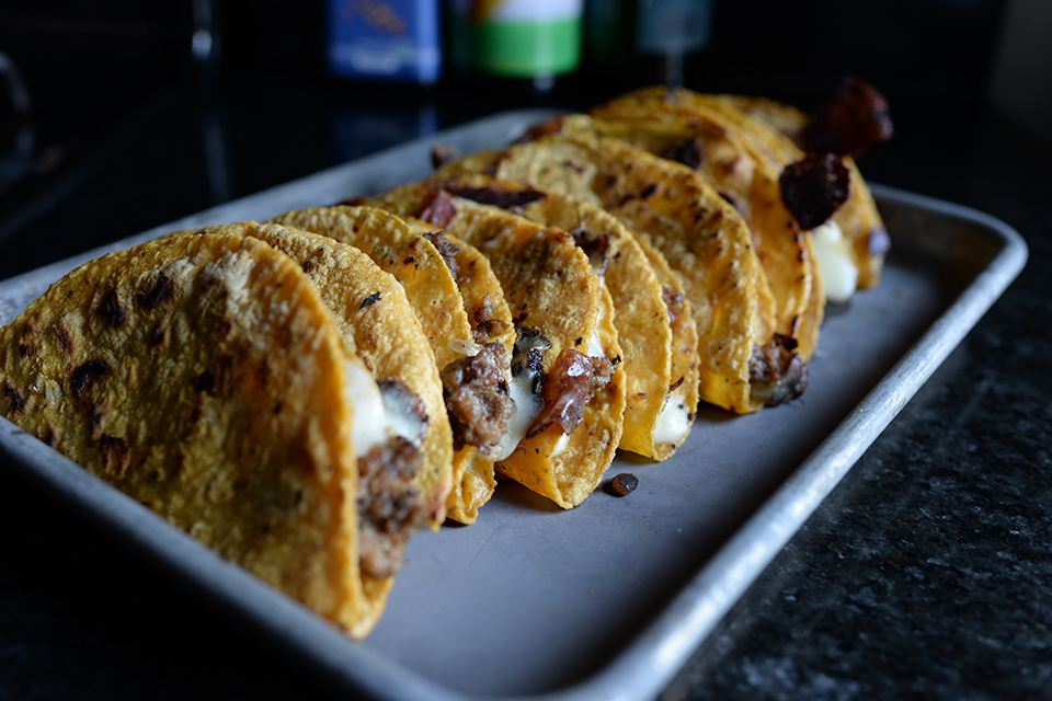 A close-up photo of a row of hard-shell tacos on a tray.