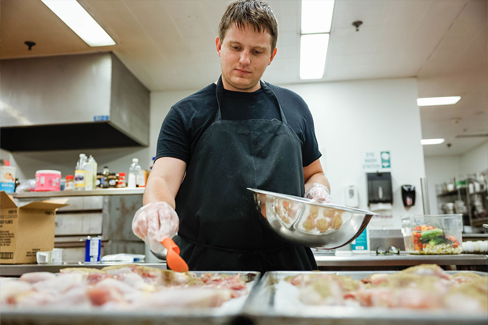 A SLU student dusts seasoning on chicken as the organization prepares meals in the Campus Kitchen for families in need. 