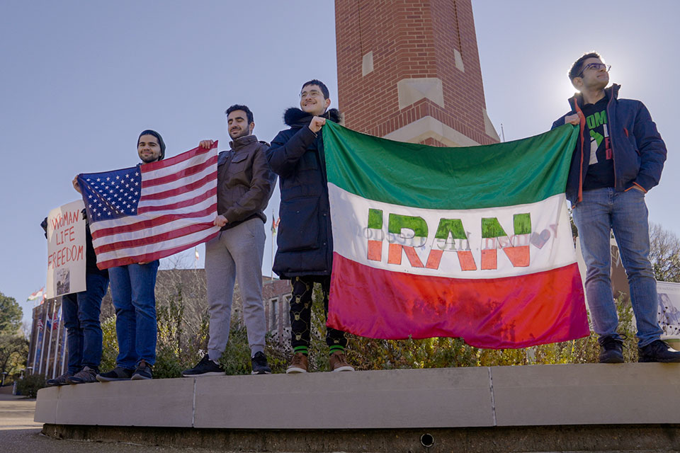 A photo of SLU community members holding American and Iranian flags at the base of SLU's clock tower during the Campus Rally for Iran.