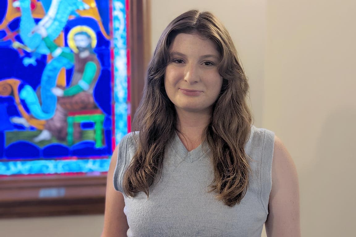 Gabrielle Chiodo takes a photo indoors in front of a stained glass window on SLU's campus. 