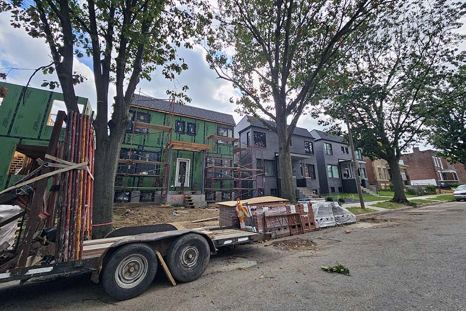A photo of a row of redeveloped houses. A truck bed with materials on it and bricks are in the foreground. 
