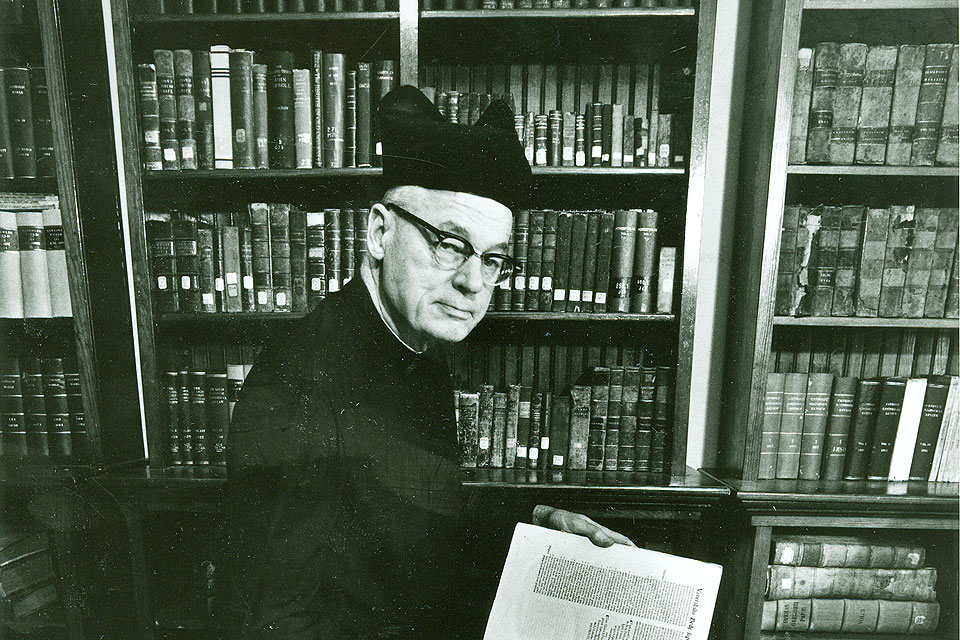 An older Claude Heithaus, S.J., in a library at the St. Stanislaus Seminary Museum in a black and white archival photo.