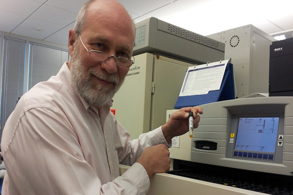 Daniel Hoft holds a test tube while working at a machine in a laboratory.