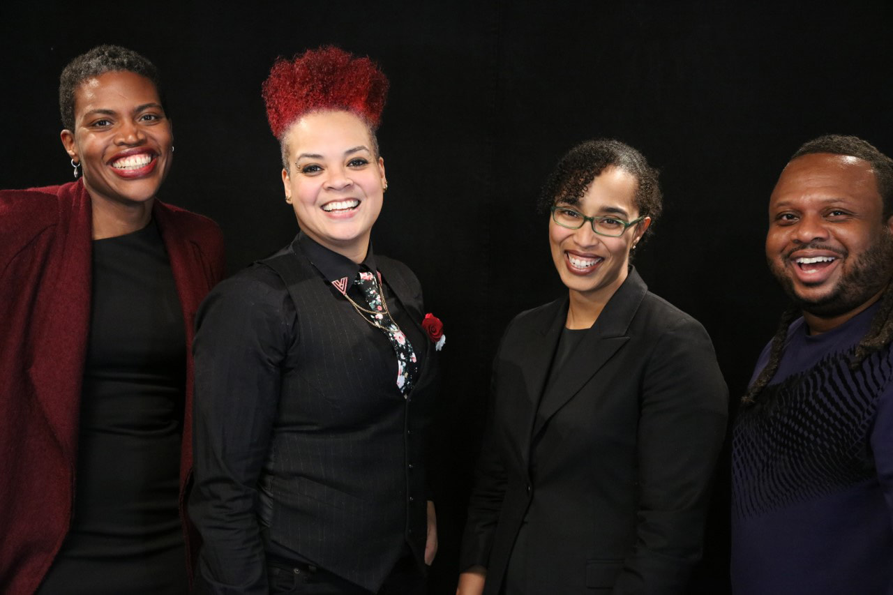 A photo of four people against a black backdrop.