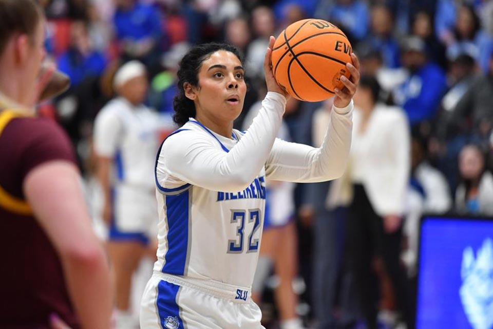 A student wearing a basketball uniform holds a basketball while looking toward the basket on the court during a game. 