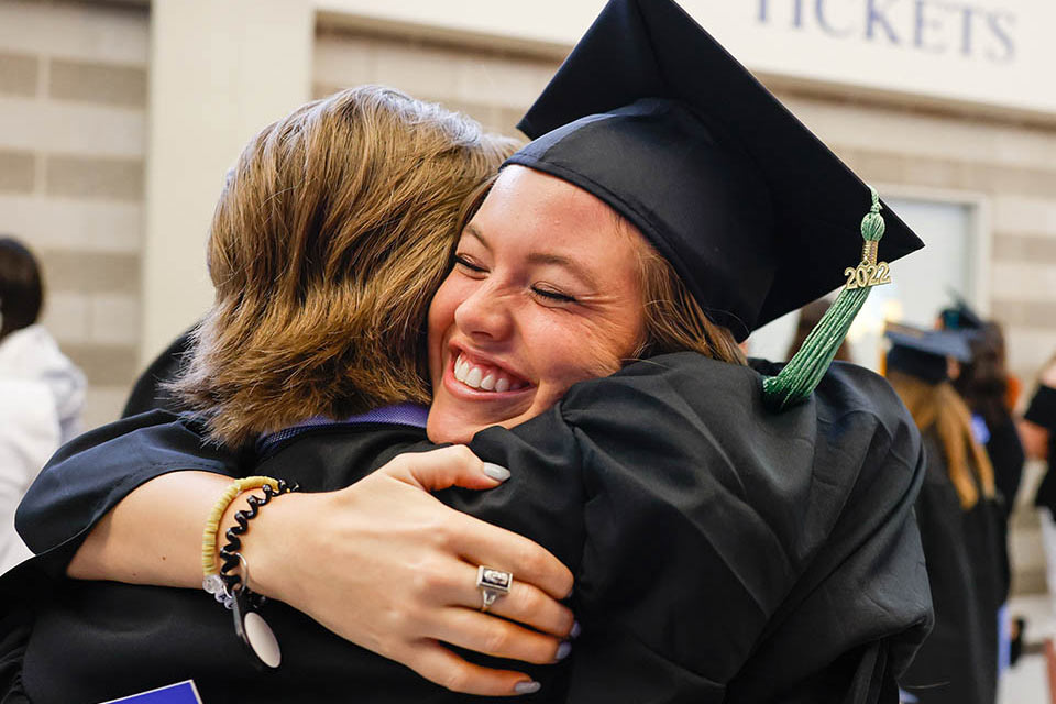 A photo of new alumna Alison Enlow embracing fellow grad James Monken in Chaifetz Arena. 