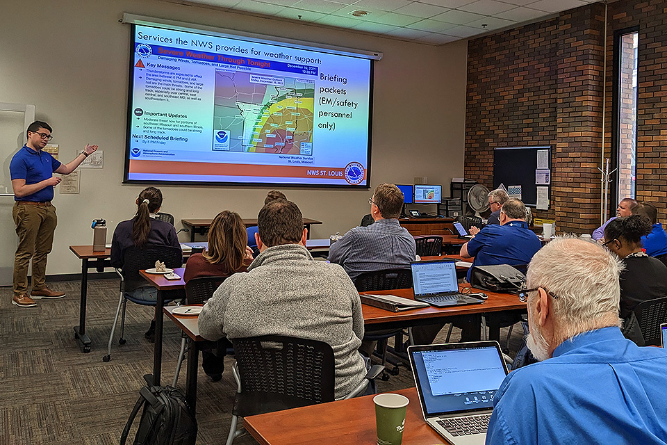 A National Weather Service meteorologist presents to a classroom full of people standing in front of a projection screen
