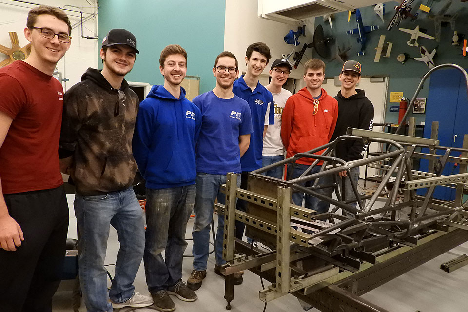 The members of the Parks Racing FASE Club gather with the chassis of their race car in Oliver Hall at Saint Louis University.
