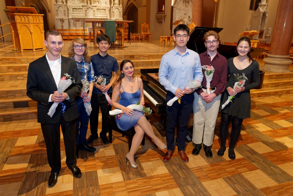 Participants in a concert in College Church stand in a group around a piano in front of the alter holding flowers