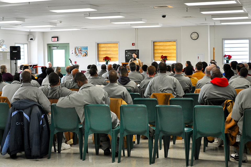 A large group listen to a speaker at a correctional facility.