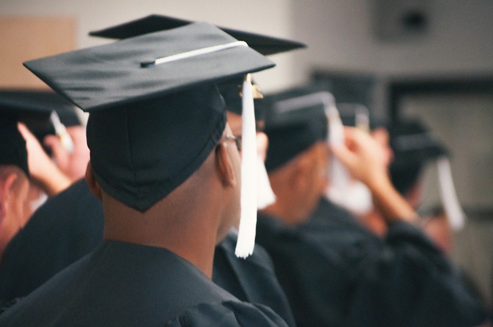 A photo of a group of graduates wearing caps and gowns shot from behind.