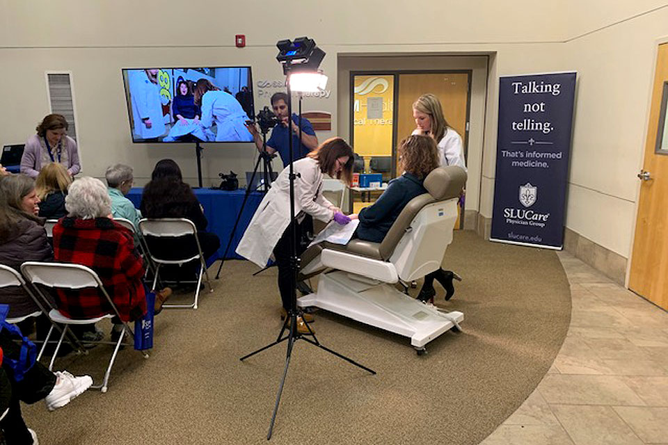 SLUCare Physicians demonstrate a dermatological technique (seated and standing figures at right) at an outreach event.