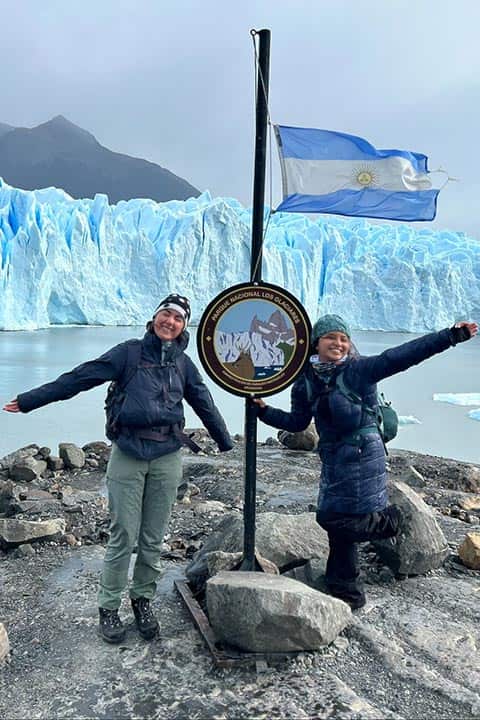 Quinn Riordan and a classmate stand in front of a sign that reads Glaciar National Park in Spanish. A flagpole with the flag of Argentina is behind the sign.