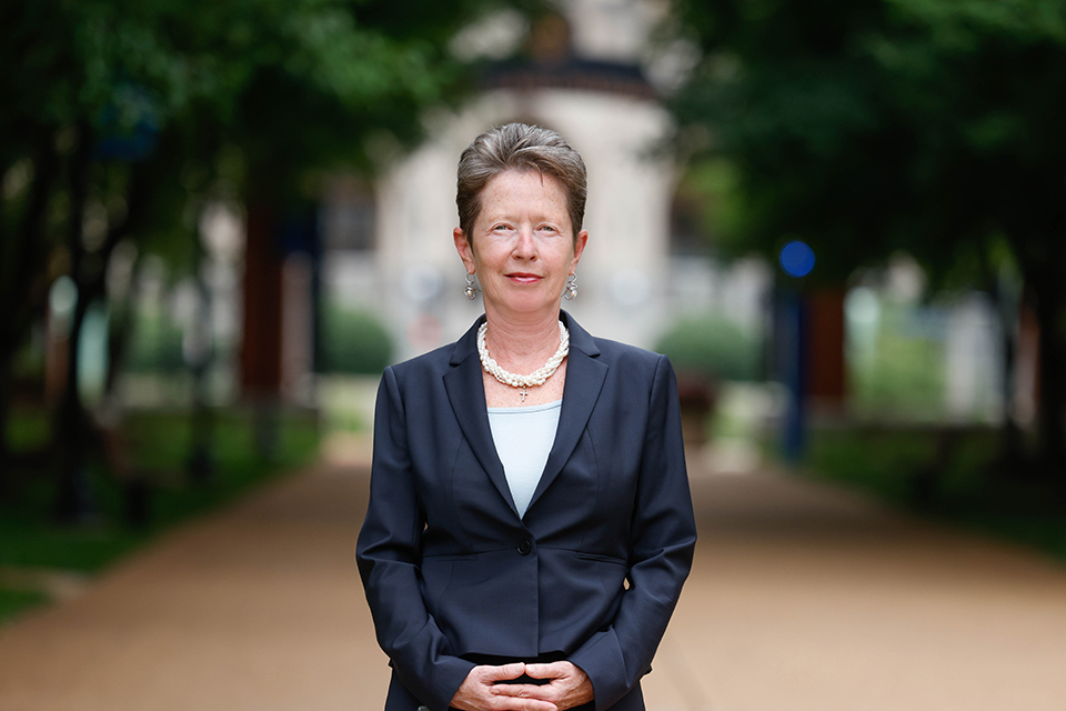 Saint Louis University pain researcher Dr. Daniela Salvemini pose for a photo outdoors during the day. The background is blurred. She wears a navy blue blazer. Her hands are clapsed at her waist.