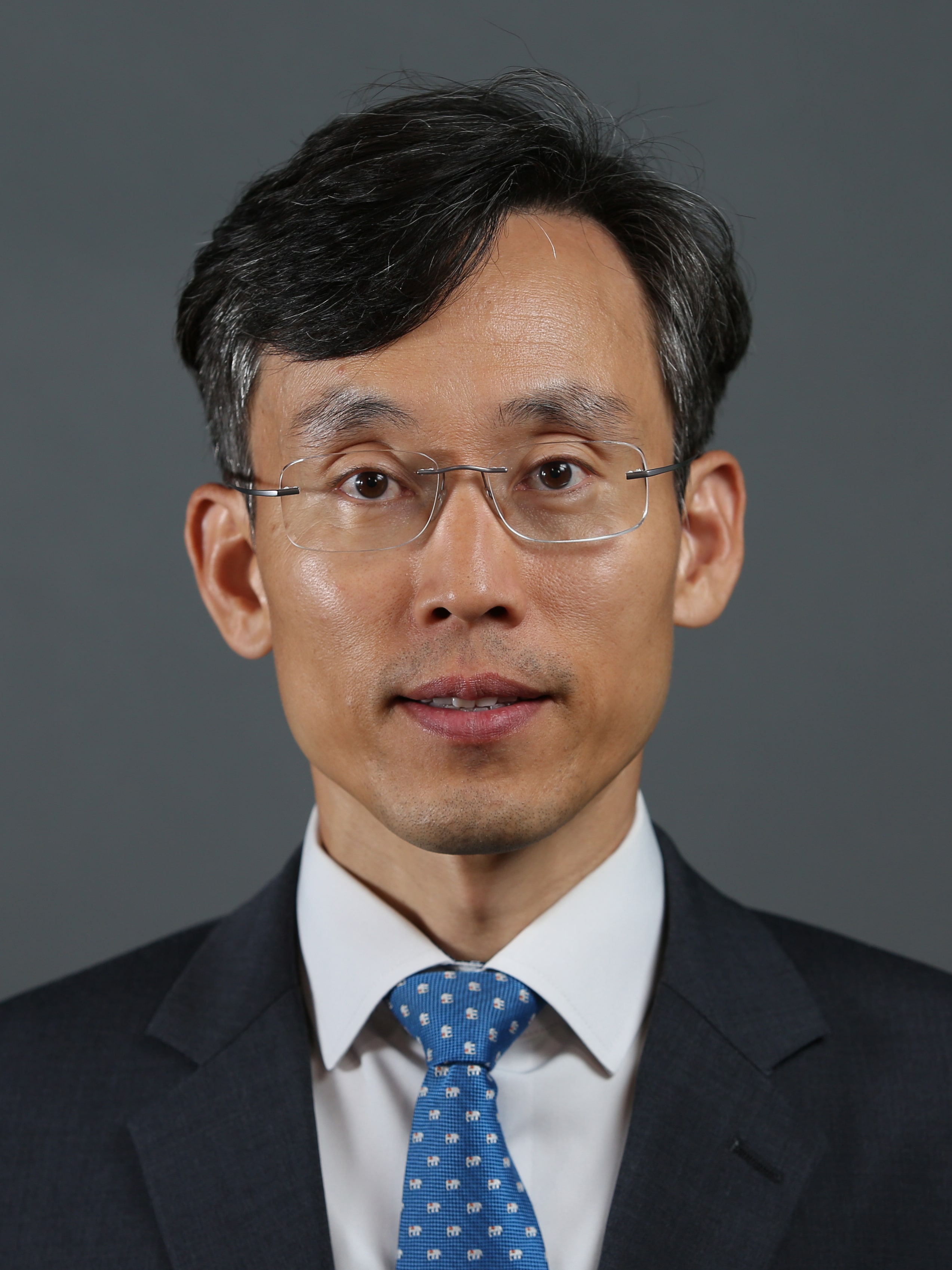 A headshot of a man wearing a black suit, white shirt and blue tie.