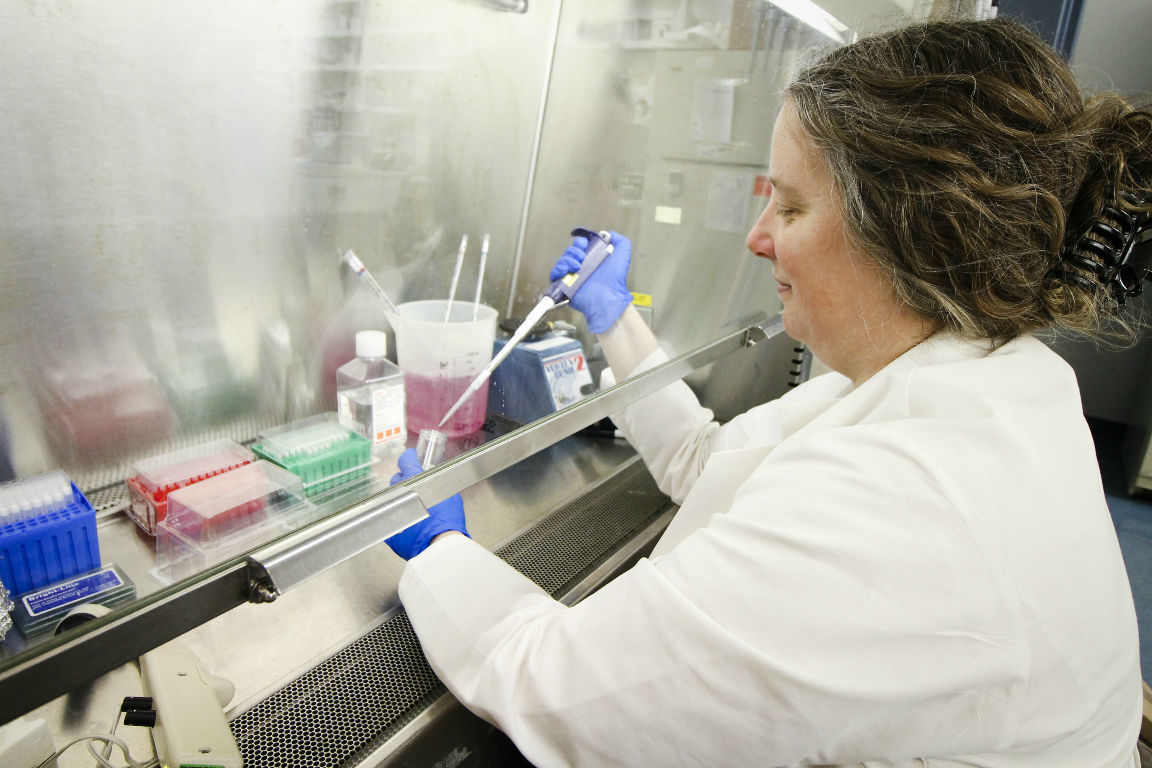 Sarah George, M.D., is shown in a lab wearing a white lab coat.
