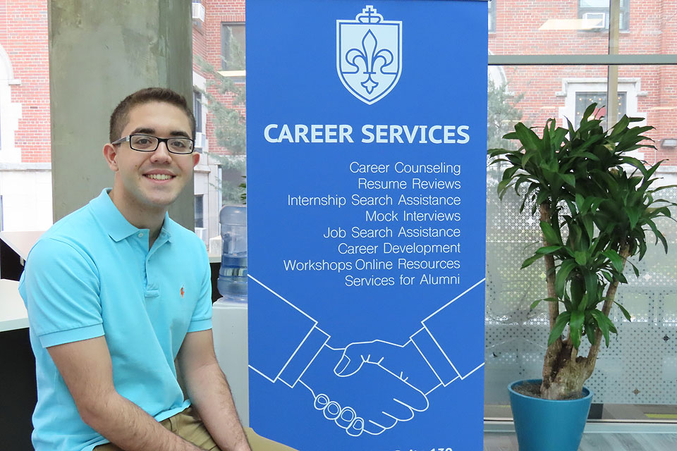 SLU sophomore Parssa Sazdar sits in the Career Services Center with a banner in the background and job hunting materials in front of him.