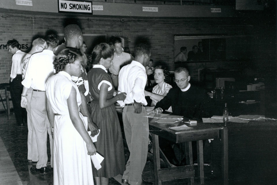 African-American students register for classes in 1951 in the West Pine Gym on the Campus of Saint Louis University in an archival, black and white photo.