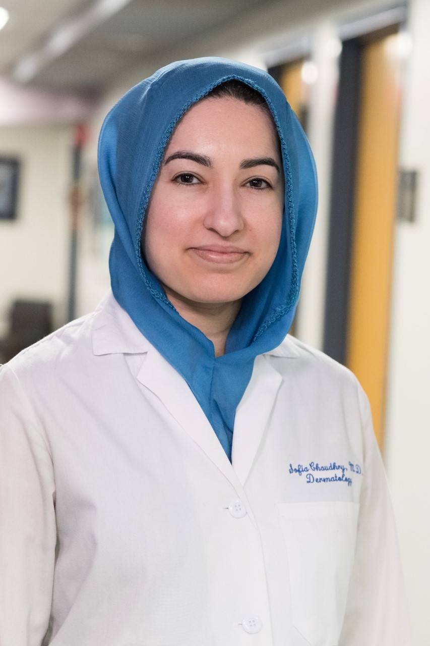 A photo of Sofia Chaudhry taken at a hospital. She wears a traditional head covering and a white lab coat.